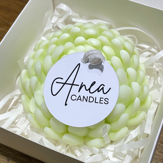 Green candle in a box with 'Anea Candles' label. PEONY SNOW PIXIE SOY CANDLE