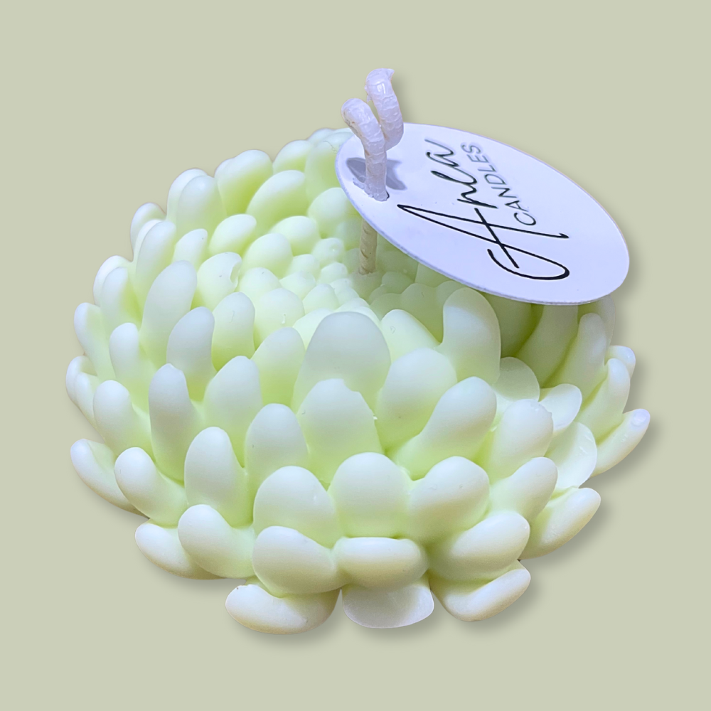 Candle shaped like a flower with a brand tag on a beige background. PEONY SNOW PIXIE SOY CANDLE