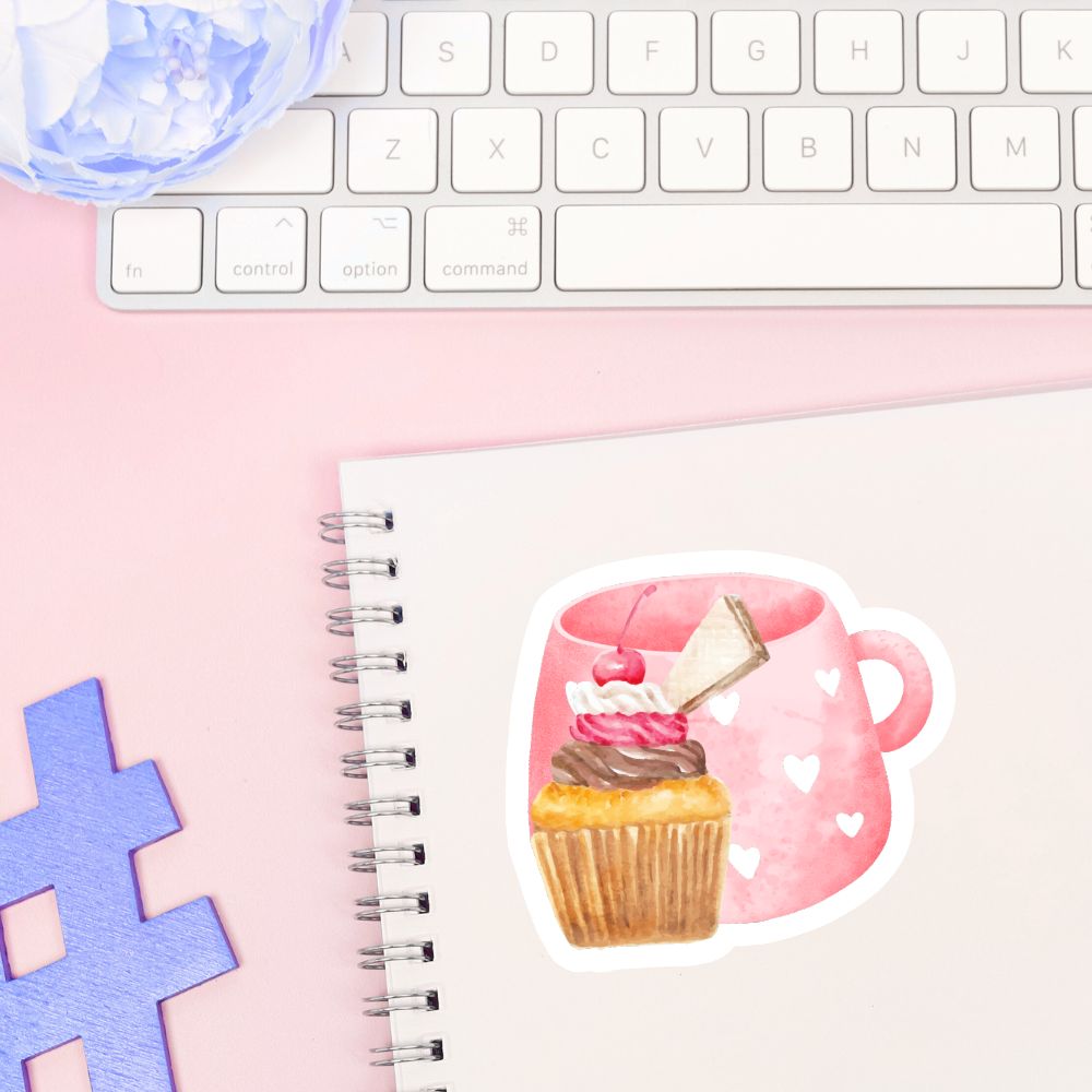 Notebook with a sticker of a pink mug with a cupcake and a piece of paper, on a pink surface with a keyboard.Cherry Cupcake Sticker