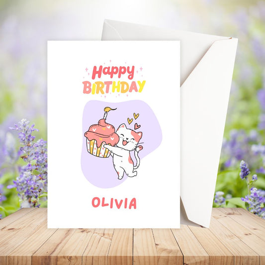 Birthday card with a cat holding a cupcake and the name Olivia on a wooden surface with flowers in the background.Cupcake Cat Birthday Personalised Card