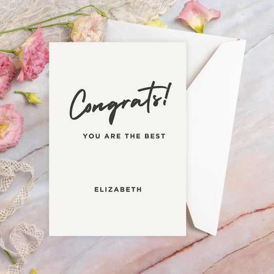 Greeting card with 'Congrats! You are the best' text on a marble surface with flowers and ribbon.ELEGANT CONGRATULATIONS PERSONALISED CARD