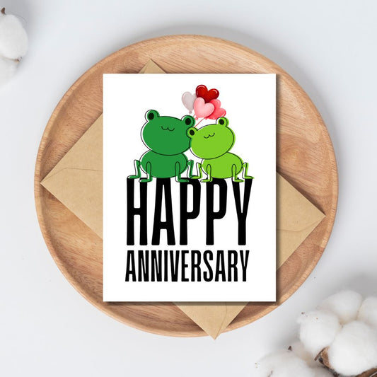 Happy Anniversary card with two frogs and balloons on a wooden plate.Frogs Anniversary Card