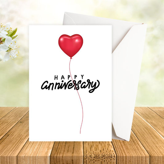 Greeting card with red heart balloon and 'Happy Anniversary' text on a wooden surface. HEART BALLOON ANNIVERSARY CARD