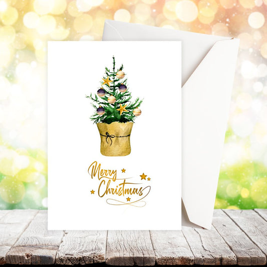 Greeting card with Christmas tree design and 'Merry Christmas' text on a wooden surface with blurred lights in the background.LITTLE TREE CHRISTMAS CARD