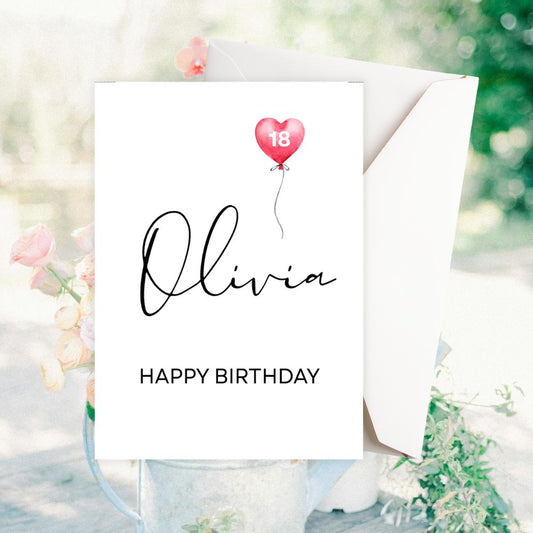 Birthday card with 'Olivia' and 'Happy Birthday' text, featuring a pink balloon, on a blurred natural background.