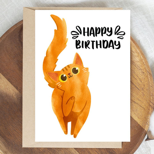 Birthday card with a cartoon cat and 'Happy Birthday' text on a wooden surface. Orange Cat Happy Birthday Card