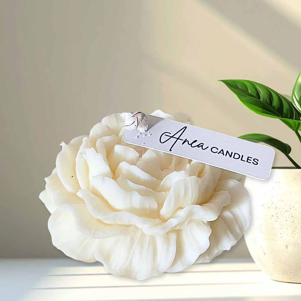 White candle shaped like a flower with 'Anea Candles' tag on a light background. PEONY CANDLE