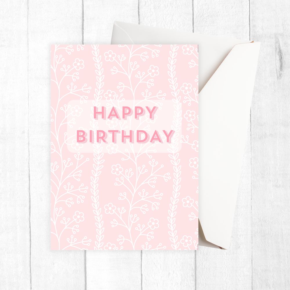 Pink birthday card with white text and floral patterns on a white wooden surface. Pastel Flower Happy Birthday Card