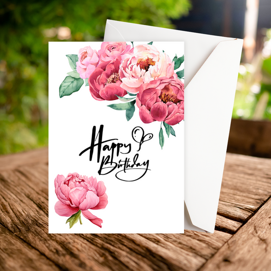 Birthday card with pink flowers and 'Happy Birthday' text on a wooden surface. PEONIES HAPPY BIRTHDAY CARD