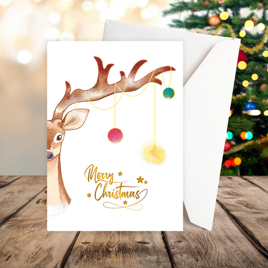 Christmas card with reindeer design and 'Merry Christmas' text, placed on a wooden surface with a blurred festive background. Reindeer Tree Christmas Card.