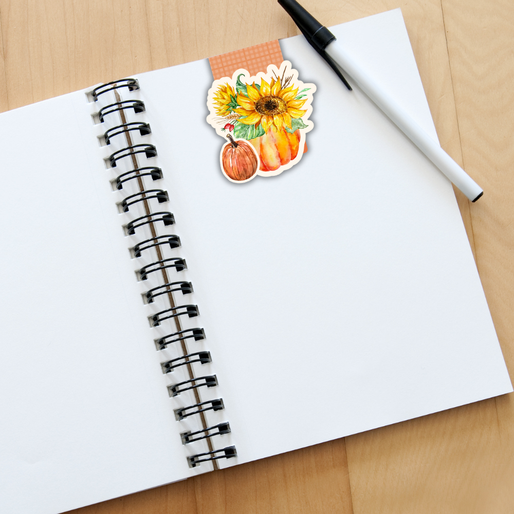 Open notebook with a sticker of a sunflower and pumpkin on a wooden surface. SUNFLOWER MAGNETIC BOOKMARK