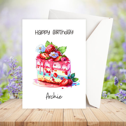 Personalised Birthday card with a colorful cake illustration and 'Happy Birthday Archie' text on a wooden surface with flowers in the background.