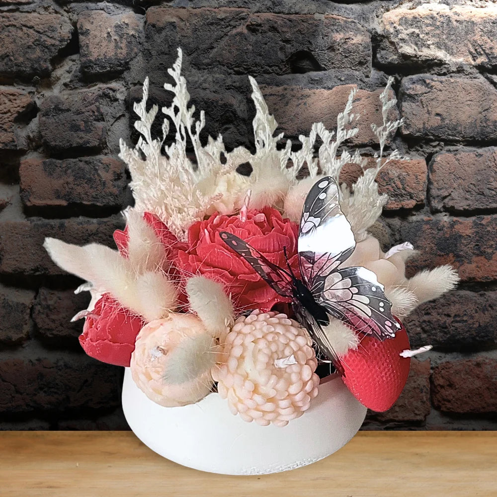 Decorative flower arrangement with pink flowers and butterfly on a white base against a brick wall.BUTTERFLY & FLOWER CANDLES CENTREPIECE
