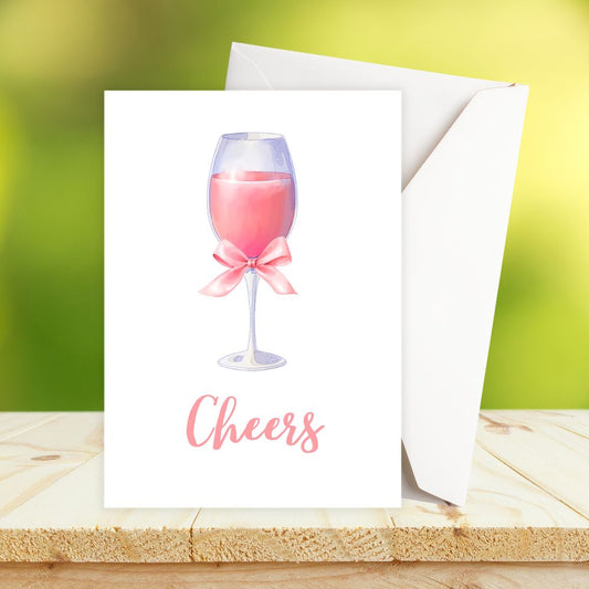 Greeting card with a pink wine glass and 'Cheers' text on a wooden surface with a green background. cheers pink cocktail glass birthday card