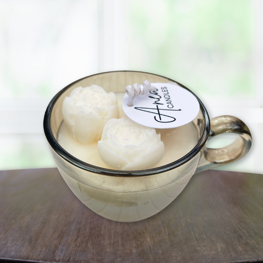 Two white candles in a glass mug with a visible brand label on a wooden surface. CHOCOLATE FRESH LINEN CANDLE