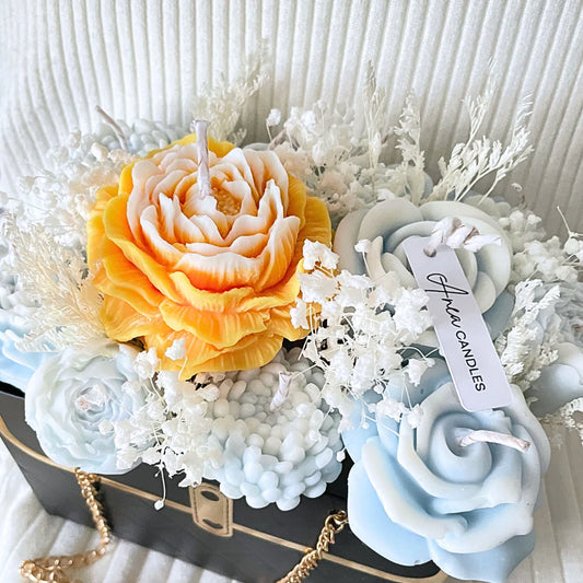 Decorative candles shaped like flowers on a textured surface with a visible brand tag. BLUE CANDLE FLOWER BOUQUET BAG