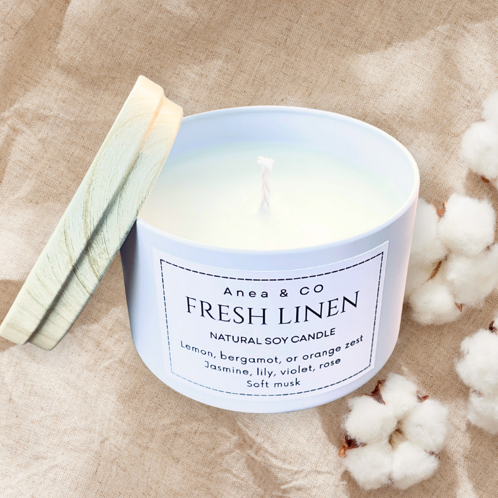 Candle labeled 'Fresh Linen' by Anea & Co on a beige fabric background with cotton fibers. fresh linen natural soy candle