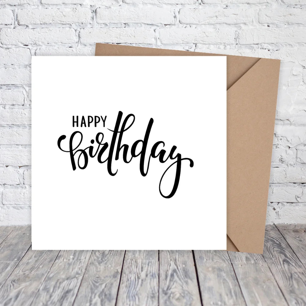 White card with 'Happy Birthday' text and brown envelope on a wooden surface with white brick wall background. HAPPY BIRTHDAY MINIMALIST CARD