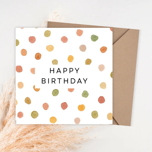 Birthday card with colorful polka dots and 'Happy Birthday' text, accompanied by a brown envelope on a light background.PASTEL DOTTED BIRTHDAY CARD