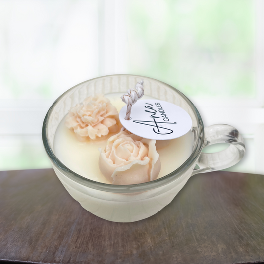 Glass mug with floral candle and 'Aimee Candles' label on a wooden surface. SANDALWOOD CINNAMON BUN CANDLE