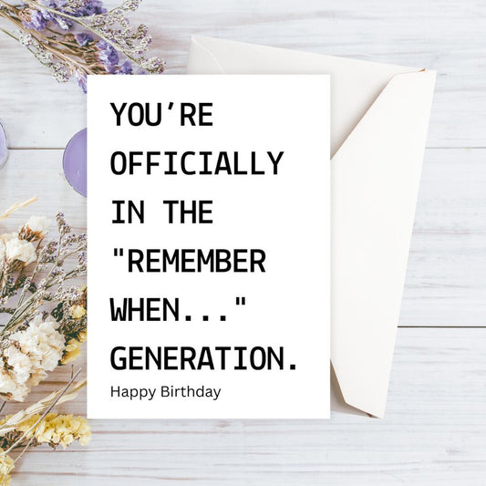 Happy Birthday card with humorous text on a wooden surface with flowers