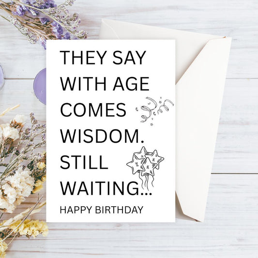 Happy Birthday card with humorous message on a wooden surface with flowers