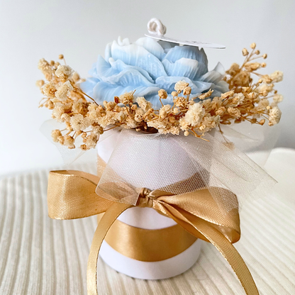 Decorative flower arrangement with blue flowers and gold accents on a white background. SANDALWOOD BLUE FLOWER CANDLE BOUQUET