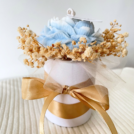 Decorative flower arrangement with blue flowers and gold accents on a white background. SANDALWOOD BLUE FLOWER CANDLE BOUQUET
