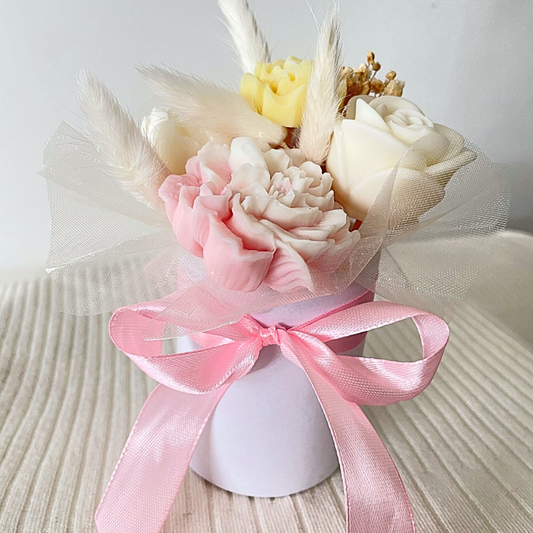 Decorative flower arrangement with pink ribbon on a textured surface. PASTEL CANDLES FLOWER BOUQUET