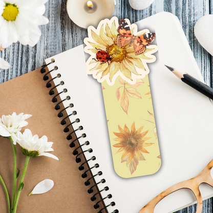 Floral bookmark with ladybug and butterfly design on a notebook with flowers and candles.AUTUMN SPARKLING BOOKMARKS II