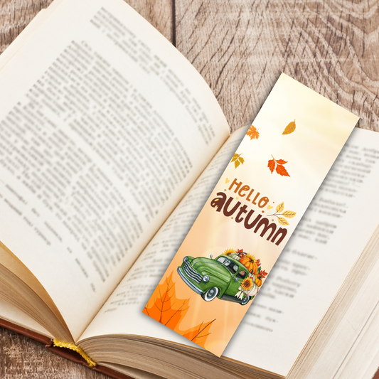 Open book with a 'Hello Autumn' bookmark featuring a green car and sunflowers on a wooden surface.