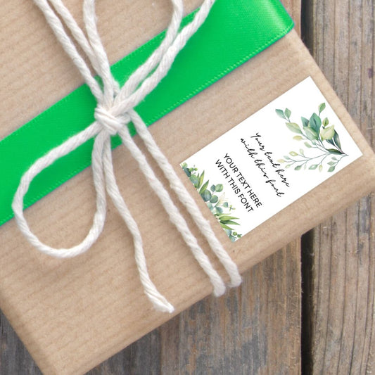 Gift wrapped in brown paper with a green ribbon and a decorative label on a wooden surface.BOTANICAL PERSONALISED GIFT TAG