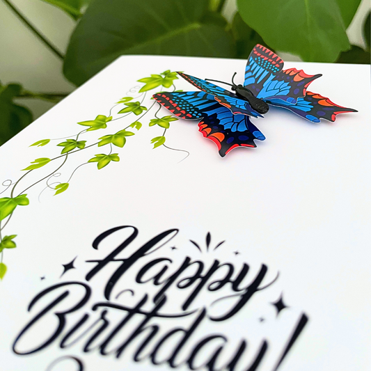 Colorful butterfly on a 'Happy Birthday!' card with green leaves in the background