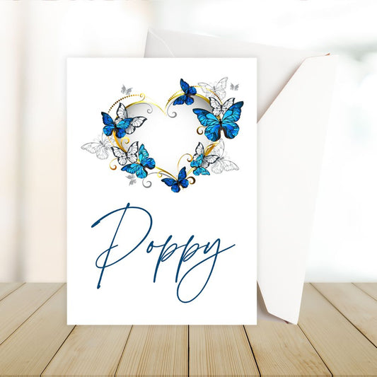 Card with blue butterflies forming a heart shape and the name 'Poppy' written below on a wooden surface.Butterflies Love Personalised Card