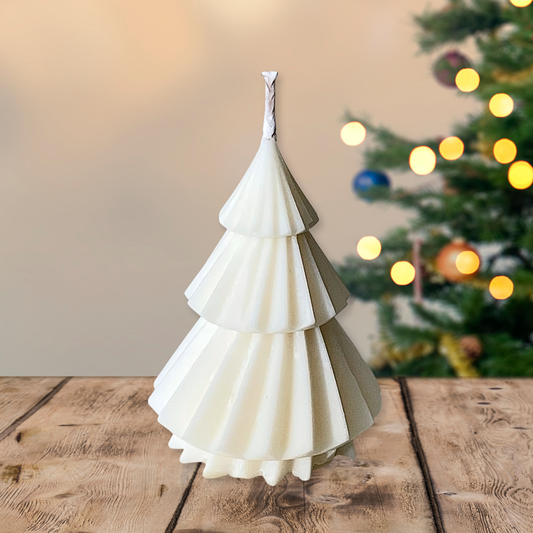 White paper Christmas tree on a wooden table with a blurred Christmas tree in the background.CHRISTMAS TREE CANDLE