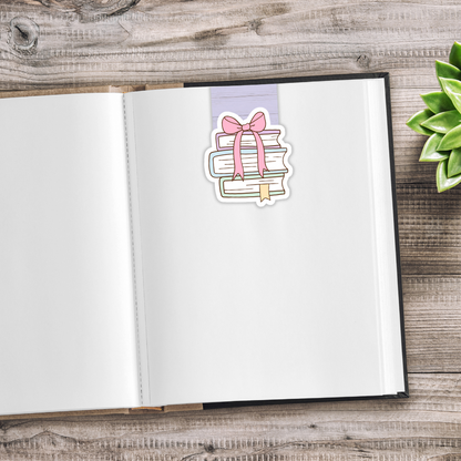 Open notebook with a decorative sticker of books and a bow on a wooden surface.CUTE BOOKS MAGNETIC BOOKMARK SET