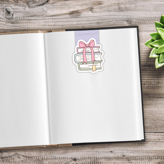 Open notebook with a decorative sticker of books and a bow on a wooden surface.CUTE BOOKS MAGNETIC BOOKMARK SET