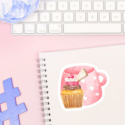 Notebook with a sticker of a pink mug with a cupcake and a piece of paper, on a pink surface with a keyboard.Cherry Cupcake Sticker