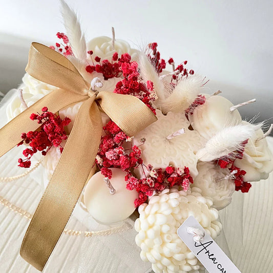 Decorative wreath with red flowers, white feathers, and a gold bow on a white background. Christmas natural soy candle