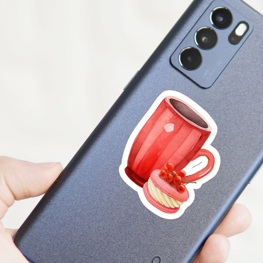 Phone case with a red mug and cookie design held by a hand. Coffee with Cranberry Cake Sticker.