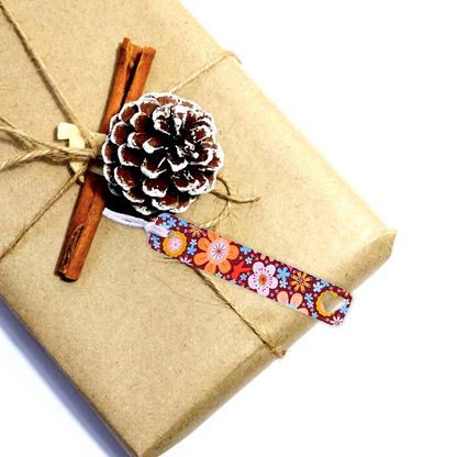 Gift wrapped in brown paper with a decorative ribbon, pine cone, and cinnamon stick on a white background. FLORAL SLIM GIFT TAG SET 1