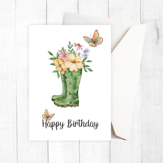 Happy Birthday card with green wellington boot holding flowers and butterflies on a white background
