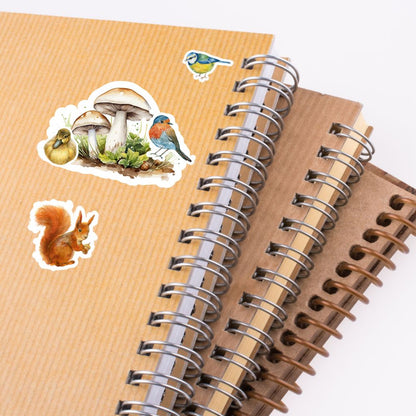 Spiral-bound notebook with stickers of a bird, mushrooms, and a squirrel on a textured surface.Forest Animals Sticker birds