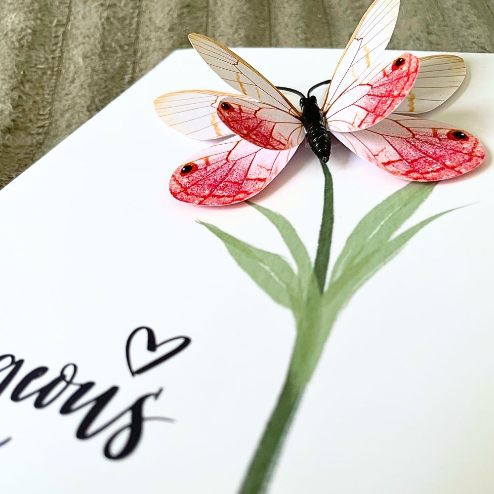 Butterfly with pink and white wings on a white surface with green leaves and black text. Gorgeous 3D Greeting Card
