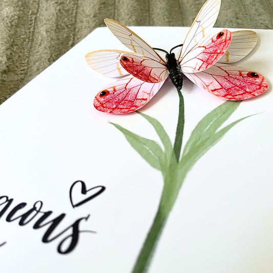 Butterfly with pink and white wings on a white surface with green leaves and black text. Gorgeous 3D Greeting Card