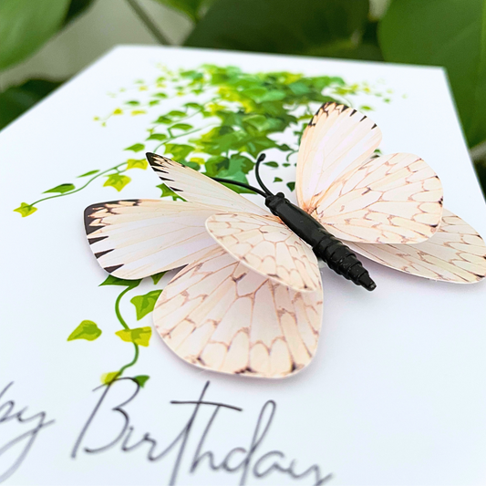Butterfly-shaped hair clip on a birthday card with greenery. Happy Birthday Cream Butterfly 3D Card
