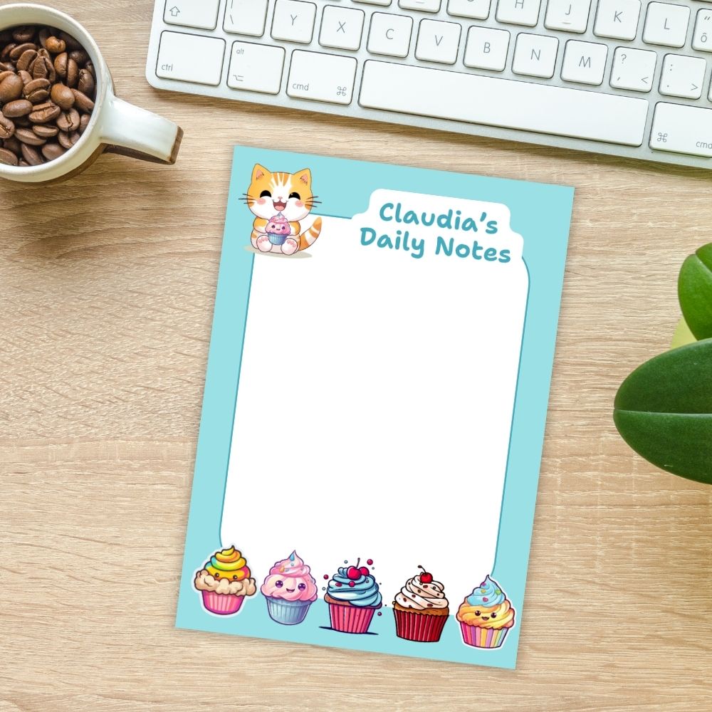 Notebook titled 'Claudia's Daily Notes' with cupcake illustrations on a desk with a mug of coffee and keyboard.KAWAII CUPCAKES PERSONALISED A6 NOTEPAD