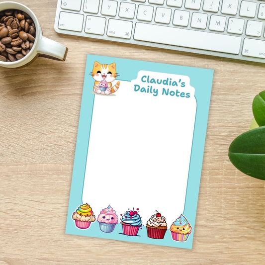 Notebook titled 'Claudia's Daily Notes' with cupcake illustrations on a desk with a mug of coffee and keyboard.KAWAII CUPCAKES PERSONALISED A6 NOTEPAD