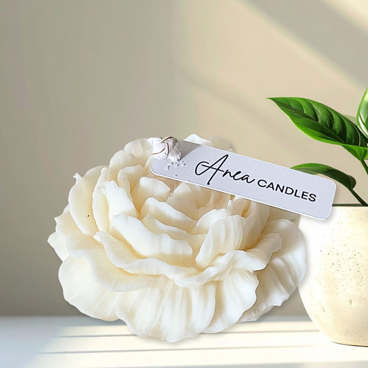 White candle shaped like a flower with 'Anea Candles' tag on a light background. PEONY CANDLE