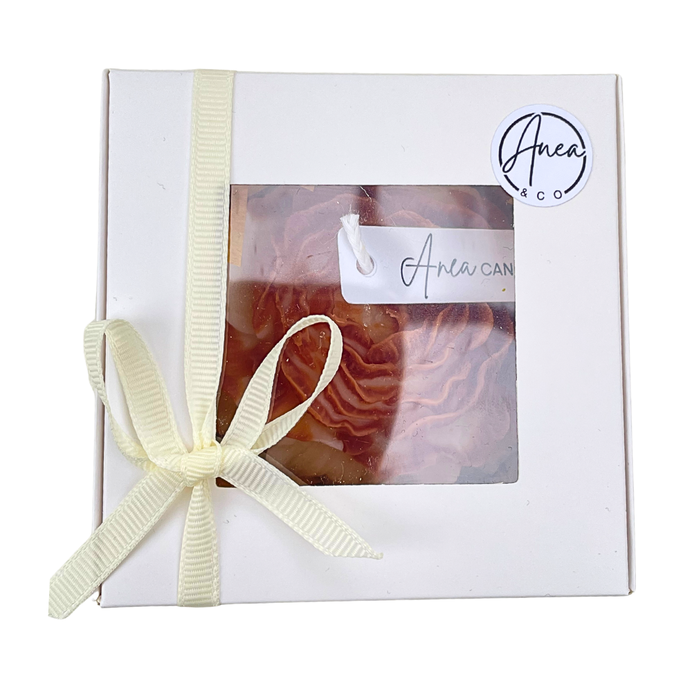 Gift box with a candle inside, tied with a ribbon, featuring the brand 'Anea & Co'. PEONY CINNAMON BUN CANDLE GIFT BOX